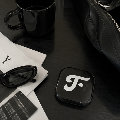 Black coaster with a white logo on a dark surface with sunglasses and papers.