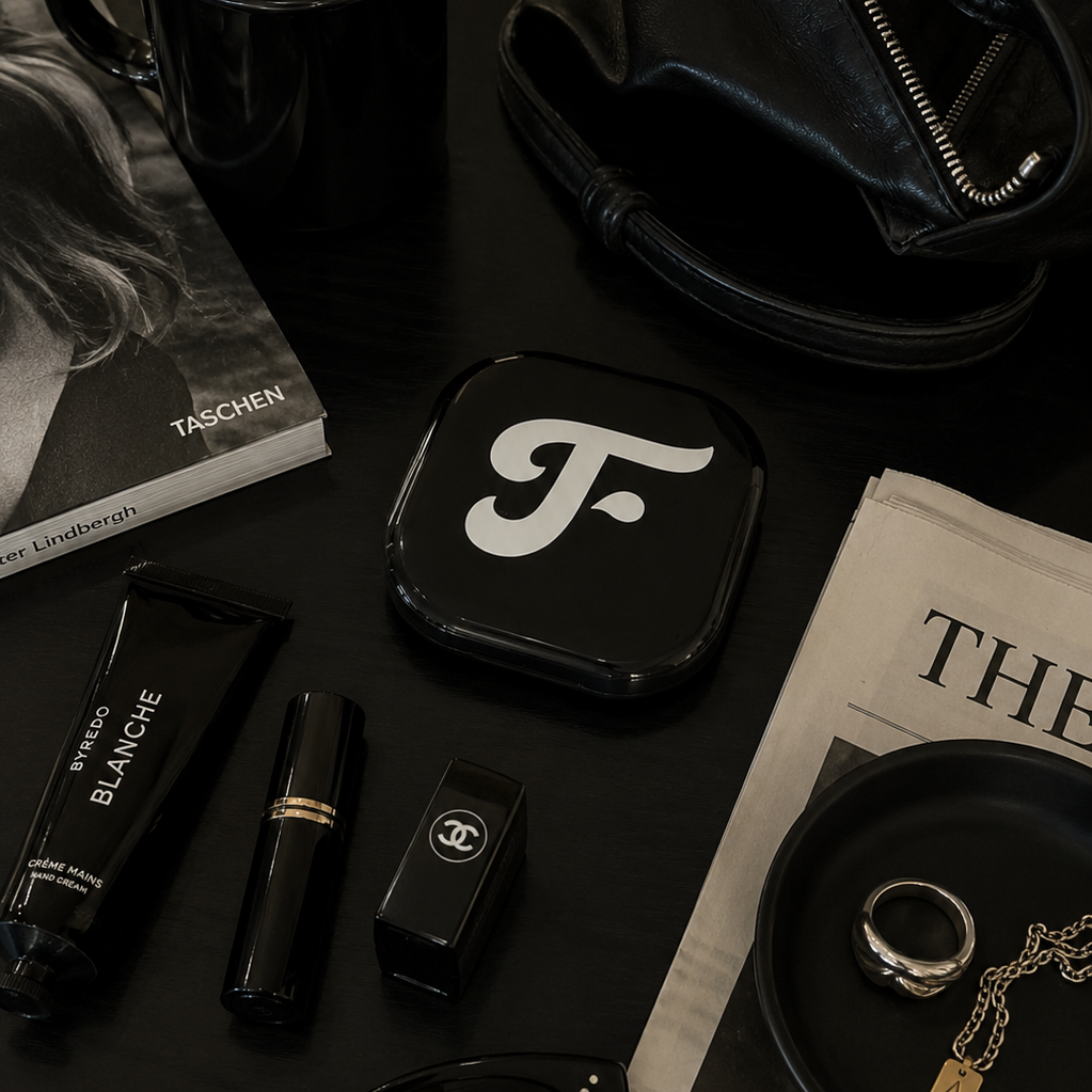 Glossy black square with white logo on a dark surface with coffee, sunglasses, and magazine.