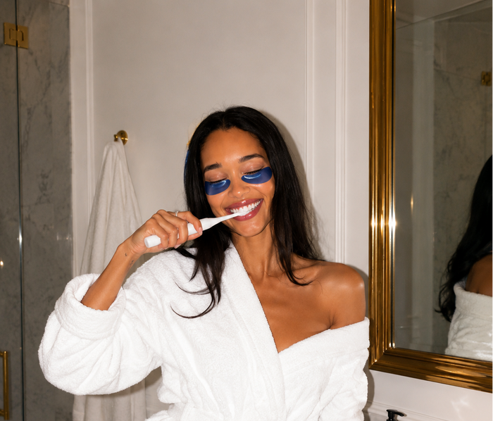 Woman brushing her teeth in a bathroom wearing a white robe.